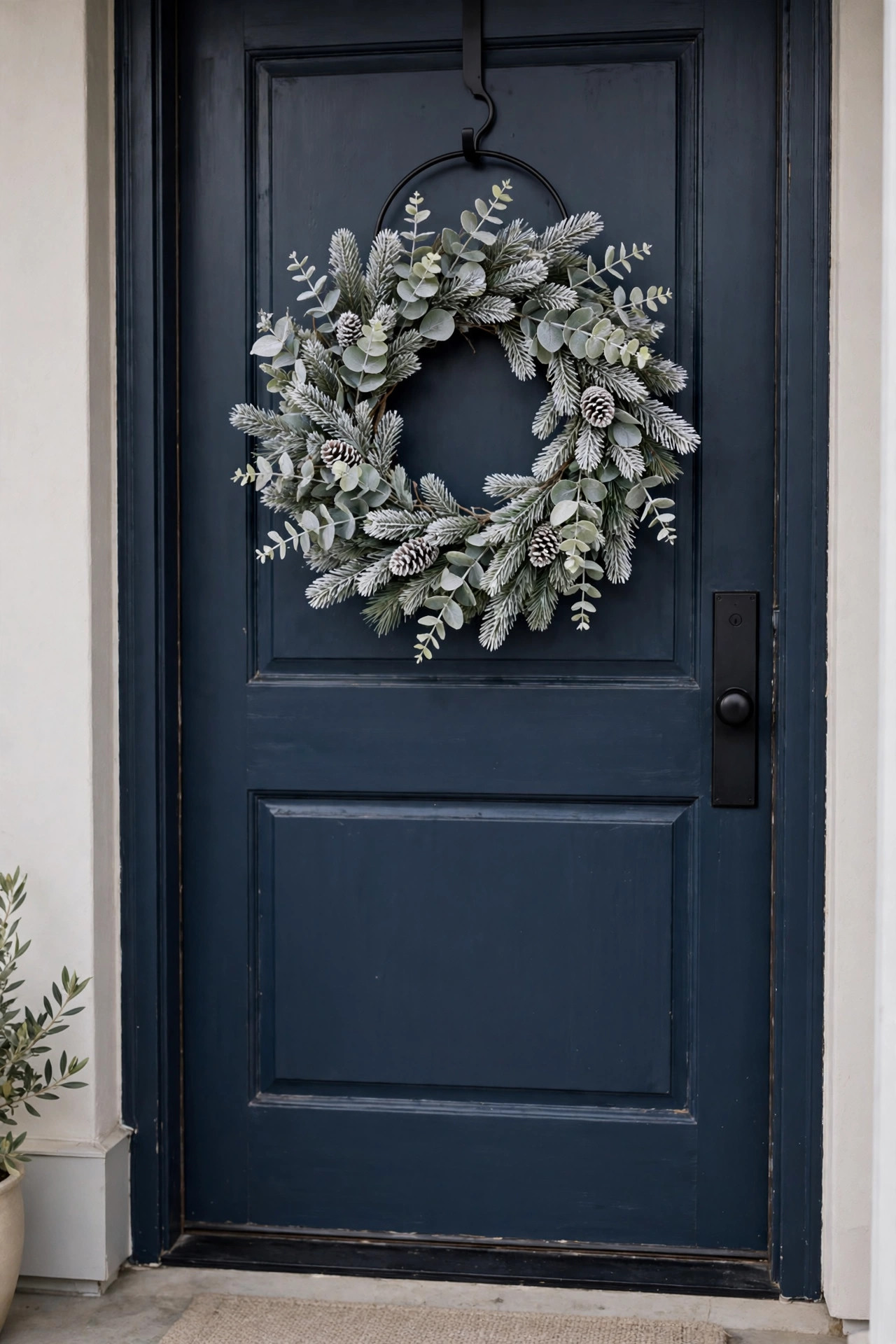 Cozy Winter Home Decor Ideas for After the Holidays 3 Simple frosted eucalyptus and pine winter wreath hanging on a dark front door with a black metal wreath hanger