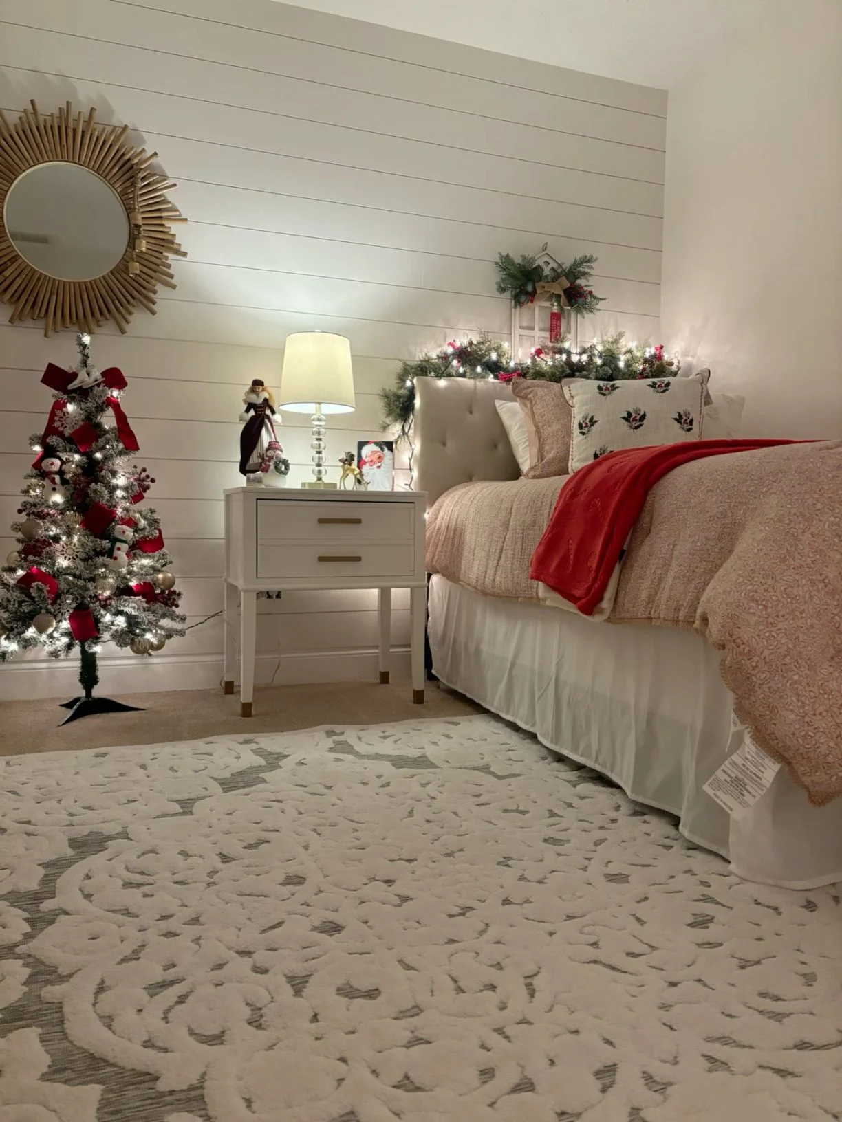 A Christmas bedroom with a bed, a tree and a large patterned rug covering the floor beside the bed