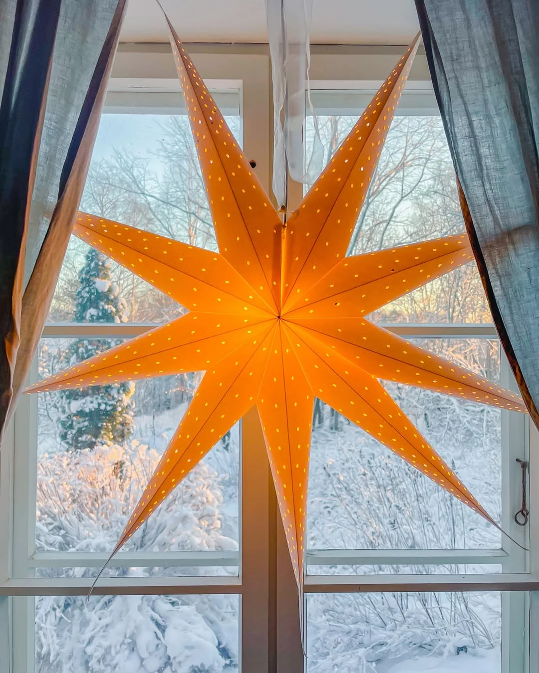 A large lit paper star hanging in a snowy window