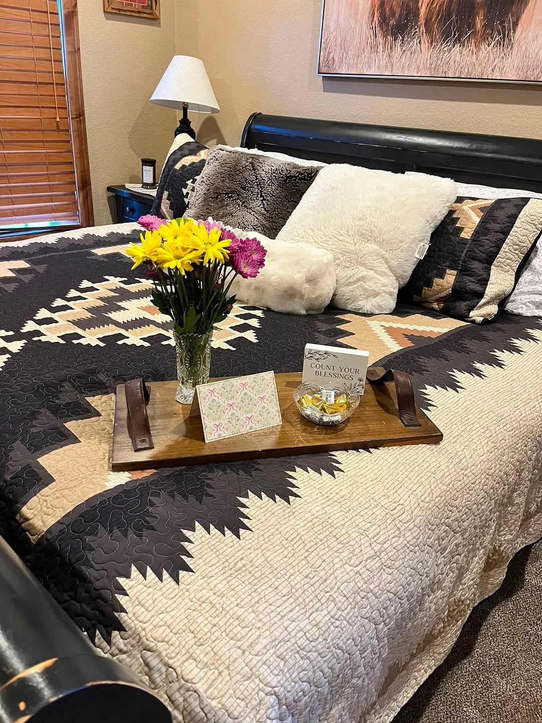 A bedroom with a bed holding a tray with flowers and cards, beside a nightstand and dresser
