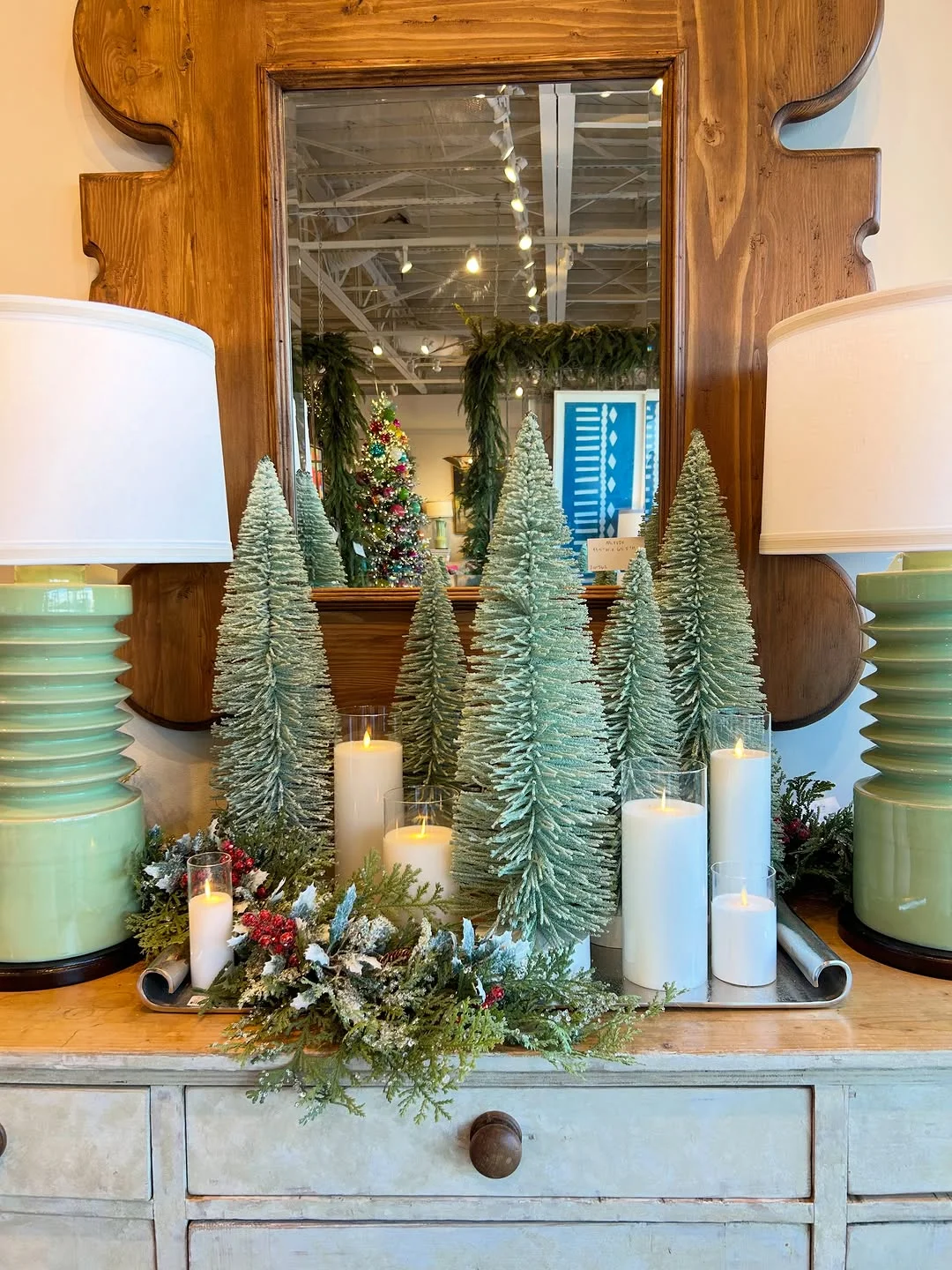 A dresser topped with bottle brush trees, candles and lamps in a showroom