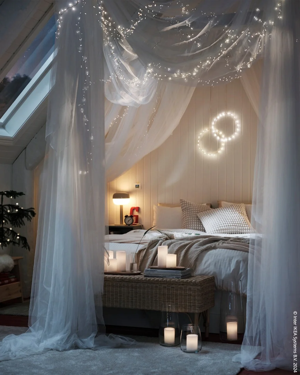 A bed under a sheer canopy with lights woven through the top, in an attic bedroom with a skylight