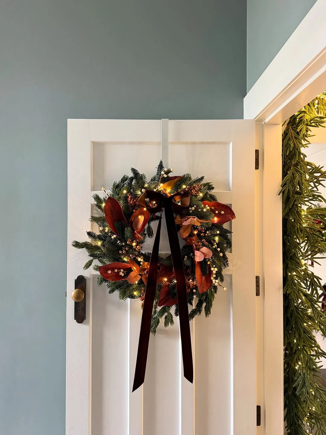 A wreath with garland hanging on a white panelled interior door